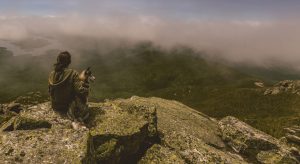 A shy girl is sitting on a cliff with her dog