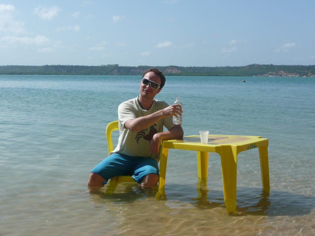 Benny relaxing sat at a table in shallow sea water because he knows language islands help him learn faster