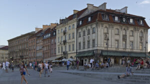 People crossing Castle Square beside historic townhouses in Warsaw