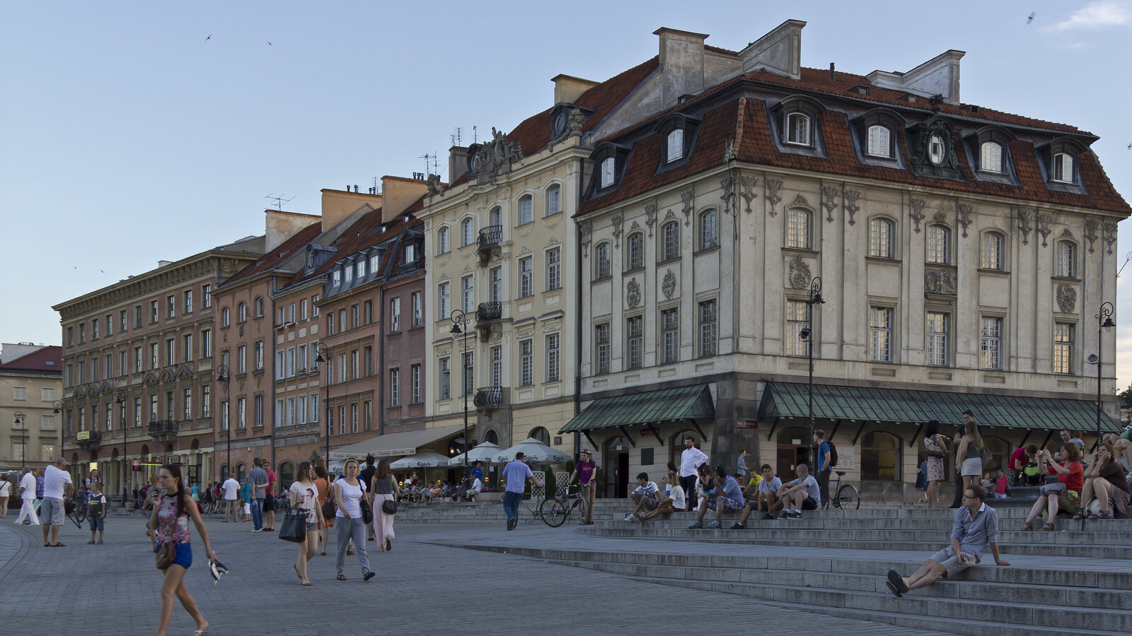 People crossing Castle Square beside historic townhouses in Warsaw