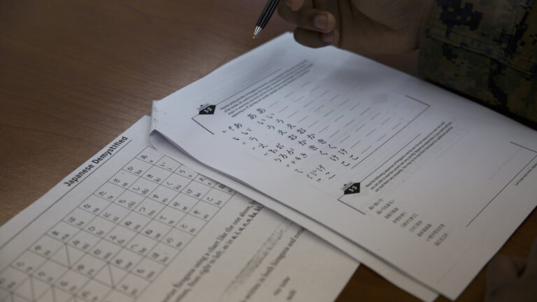 Japanese kana practice sheets beside a learner’s hand and pen.