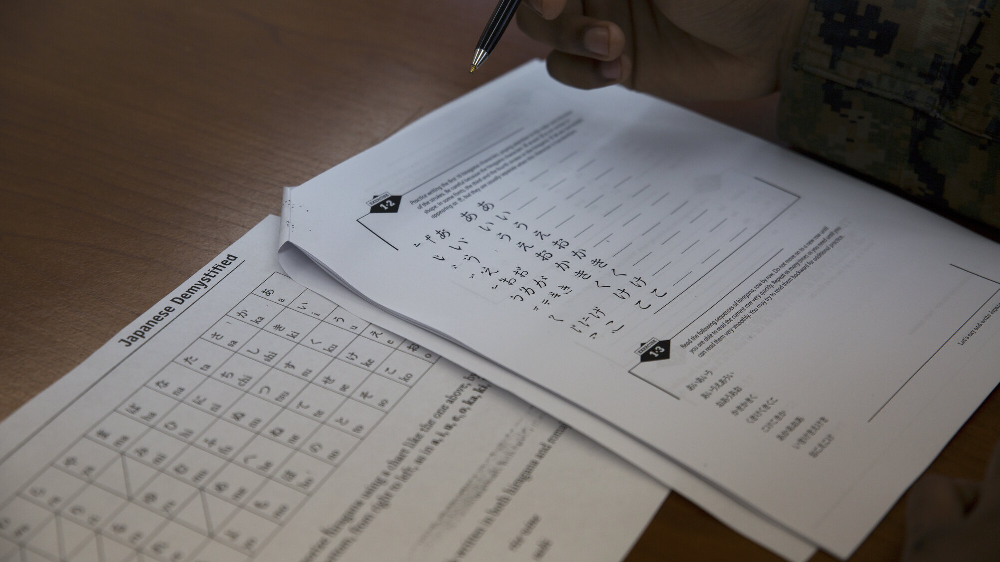Japanese kana practice sheets beside a learner’s hand and pen.